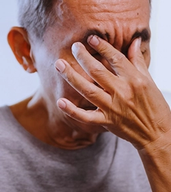 Man covering eyes due to blurred vision caused by muscle imbalance, treated with botulinum toxin
